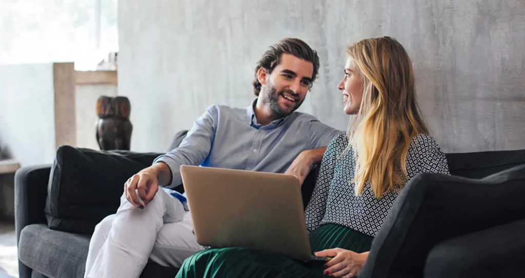 a man and woman sitting on a couch looking at a laptop